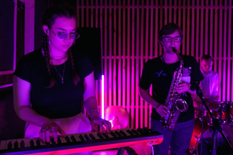 A band performing live music with a keyboard and saxophone under colorful stage lighting.