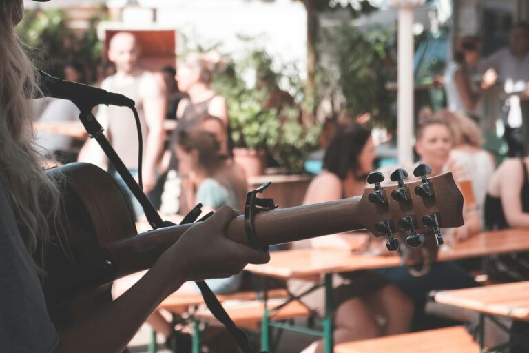 An artist plays guitar outdoors at a lively festival. Blurred crowd in background.